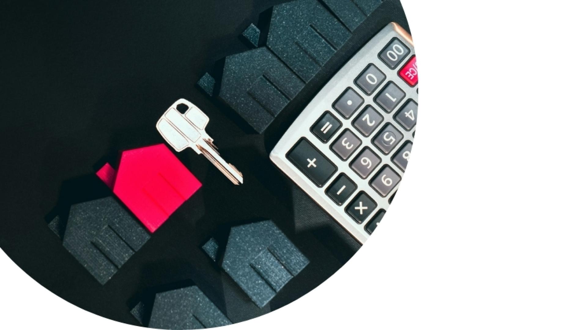 little cardboard 2d black houses, with one red, and a house key with a calculator on a black desk
