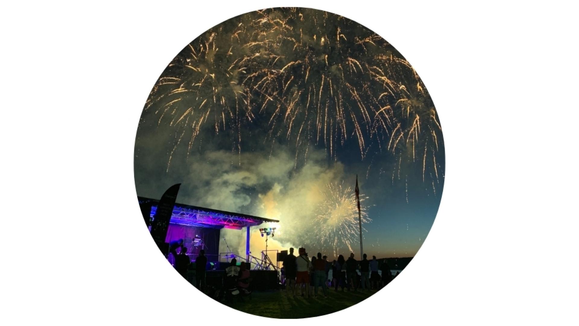 fireworks over the river, while a music show is playing during an outdoor celebration