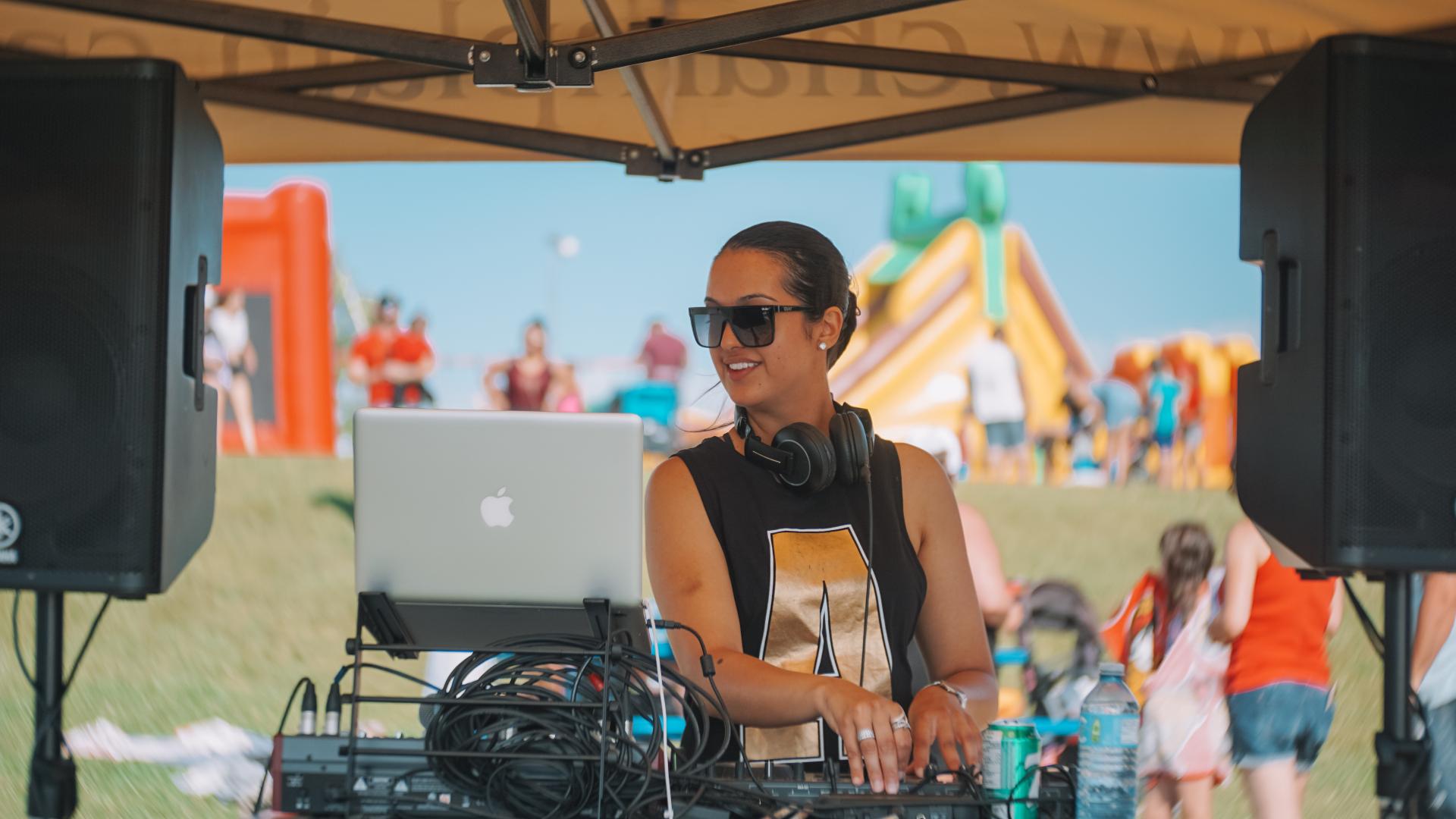 DJ performing outdoors with inflatable games and family activities in the background.