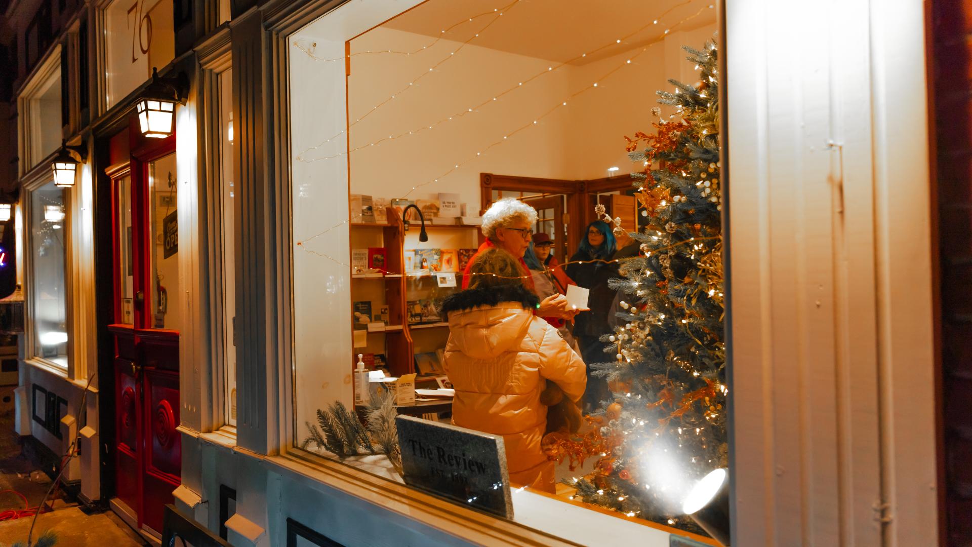 People gathered inside a decorated storefront with a Christmas tree and holiday lights during the Christmas parade evening.