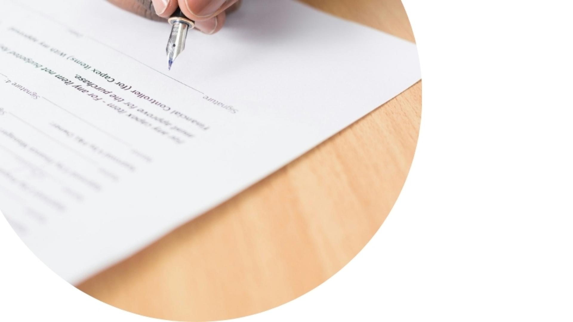 someone signing a filled form with a pen on a wood table