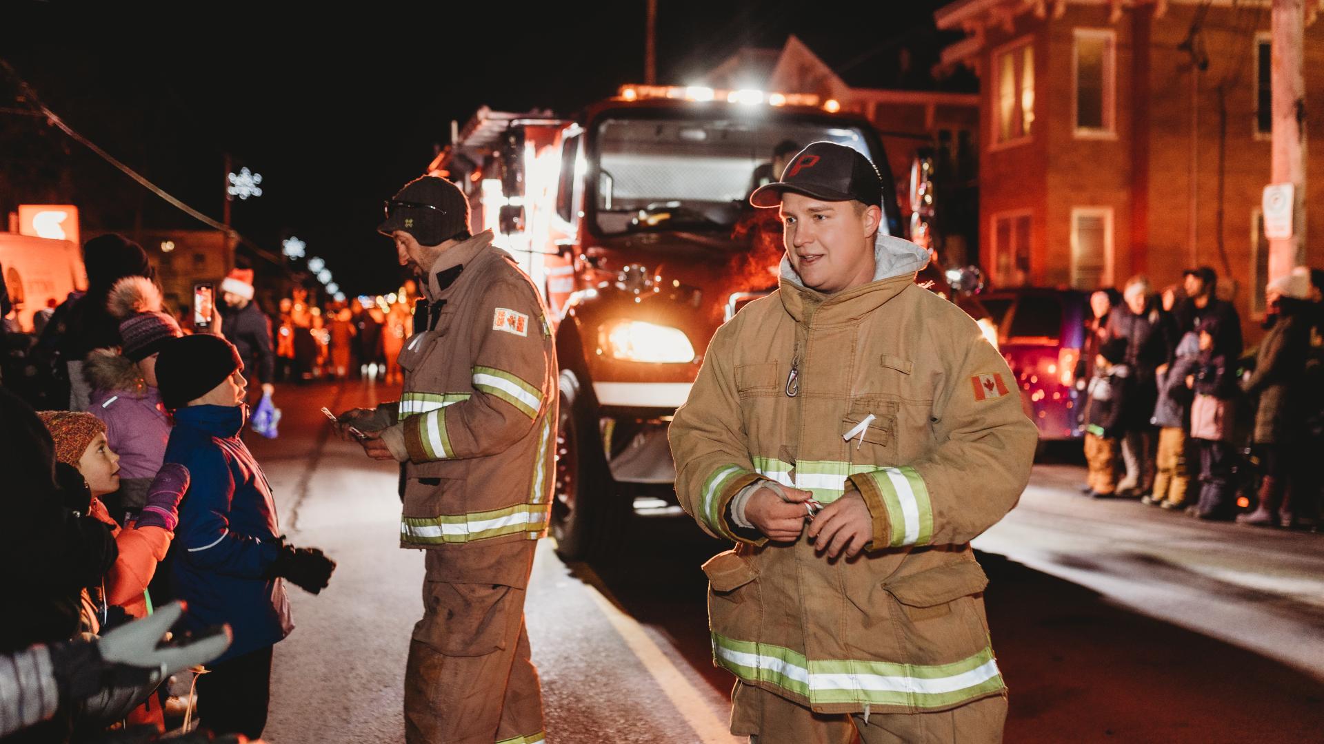 Firefighters walking along the Christmas parade route while greeting children and spectators beside a fire truck