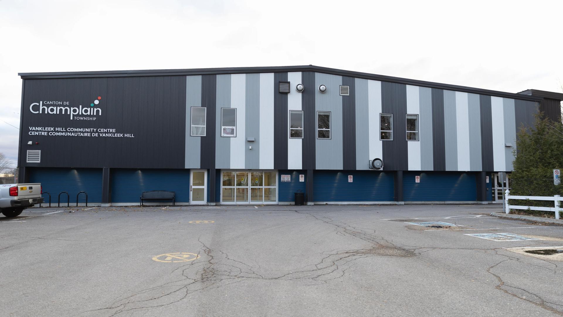 Exterior view of the Vankleek Hill Arena featuring modern blue, grey, and white metal siding, the Township of Champlain logo, and the main public entrance.
