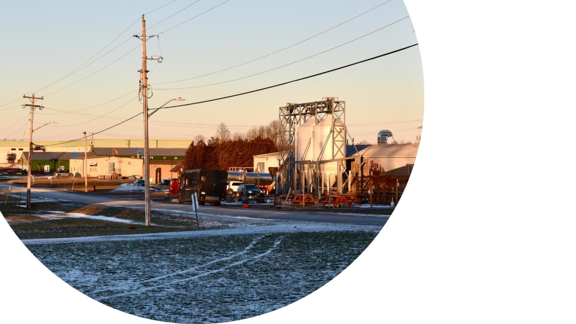 Industrial area featuring commercial and manufacturing buildings, utility poles, and a roadway during winter,