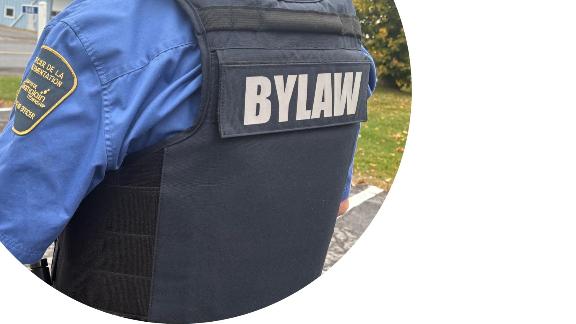 Close-up of a Municipal Law Enforcement Officer wearing a blue Township of Champlain uniform shirt with "Bylaw" printed on the back.
