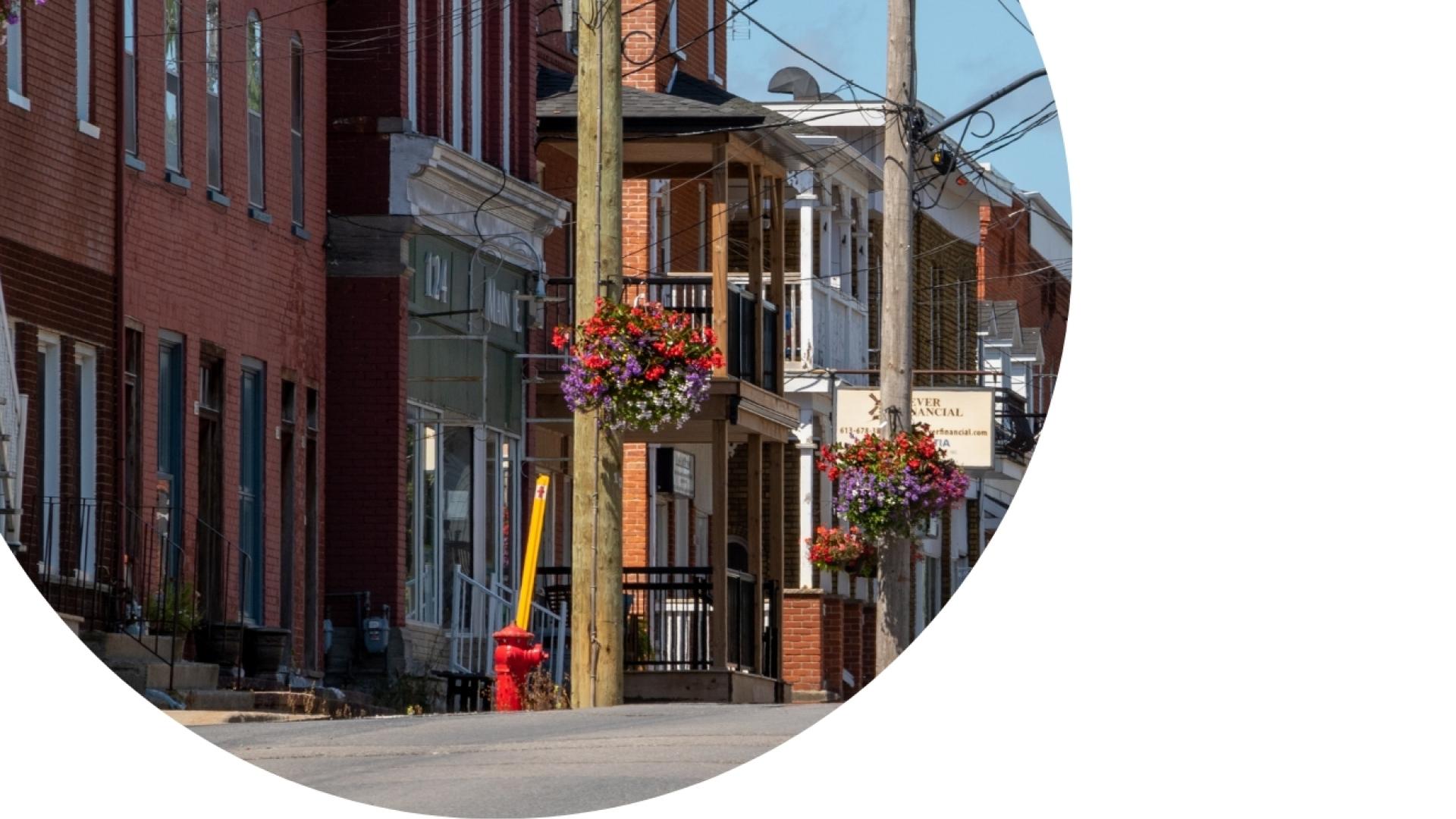 Historic downtown streetscape featuring brick commercial buildings, storefronts, hanging flower baskets.