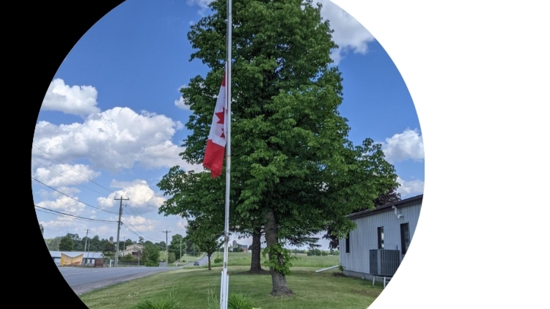 Canadian flag flying on a flagpole beside a roadway, framed within a black and teal graphic design.