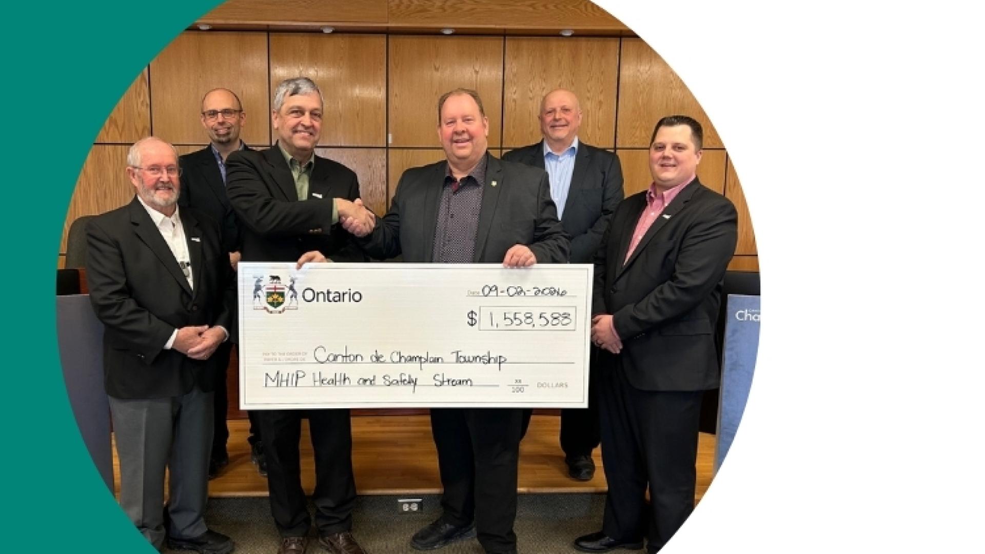 Seven people hold a large cheque in a formal setting with a Canadian flag.