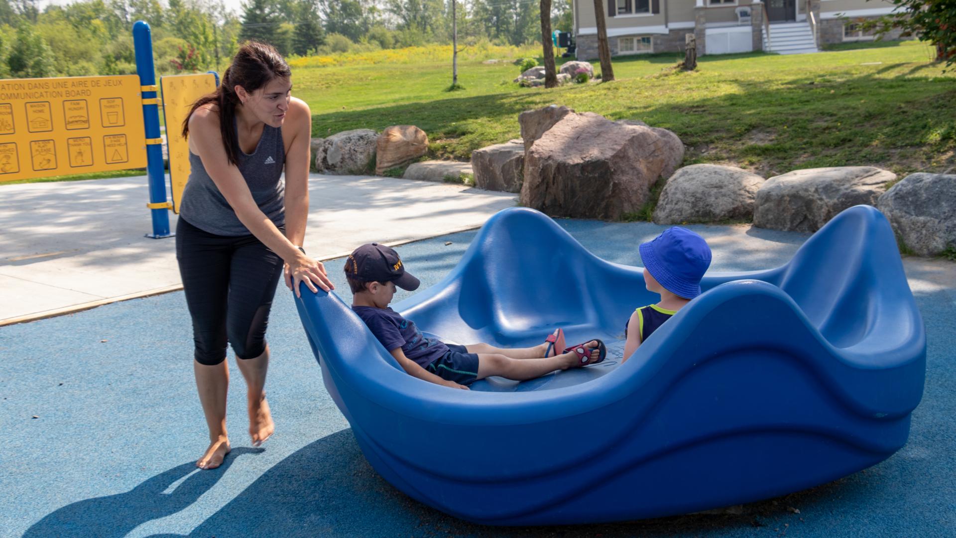 Adult and child using an accessible spinning play structure at Sacha's Park playground.