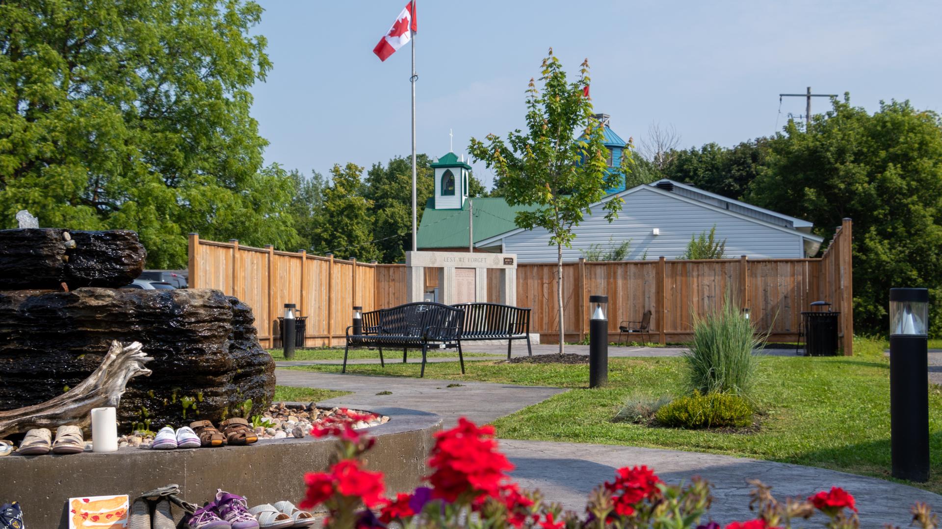 Town Square Park featuring benches, a decorative water fountain, Canadian flags, and a commemorative monument surrounded by landscaped green space.