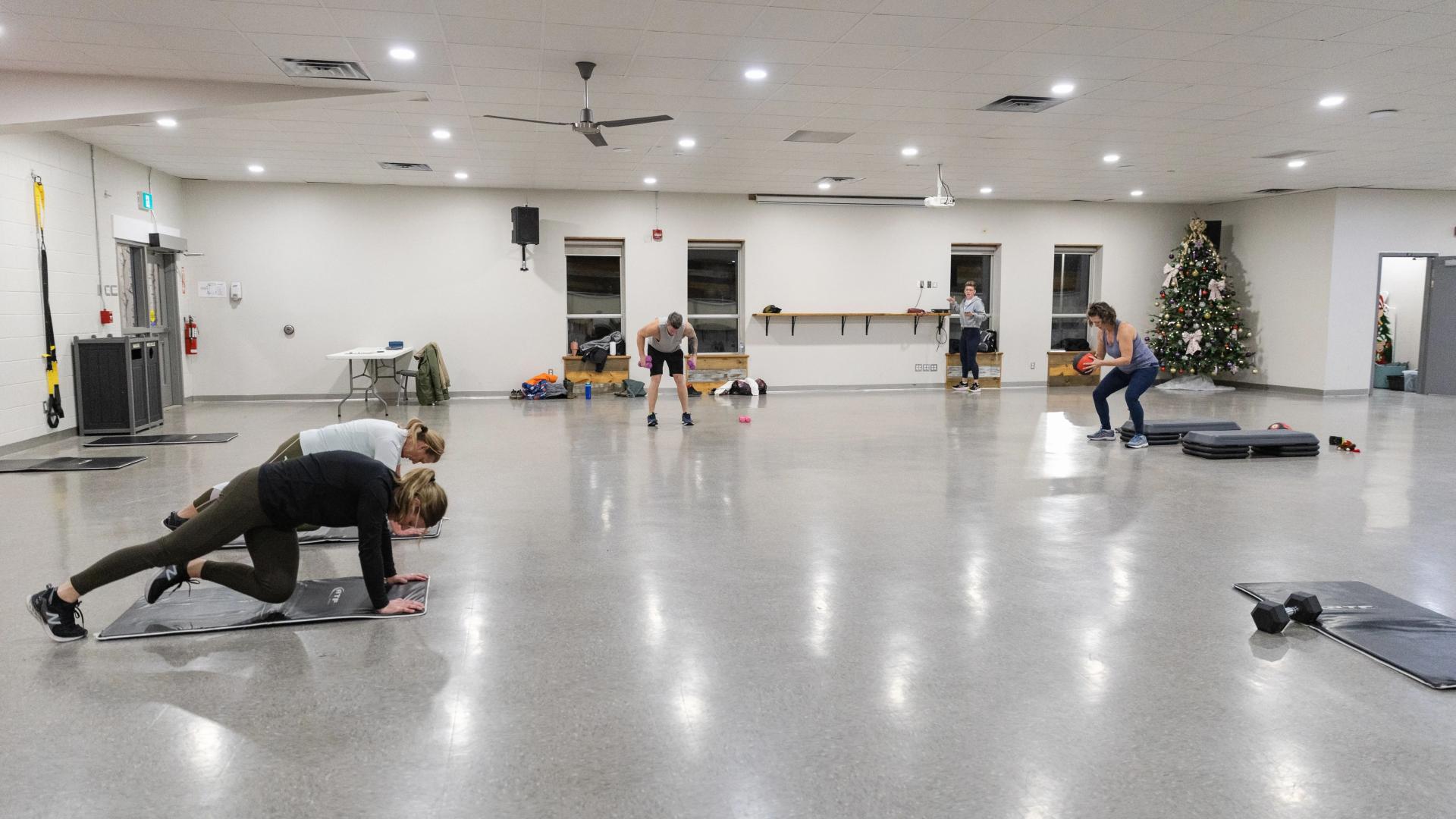 Community hall with participants taking part in a fitness class, exercising on mats in a large open room.