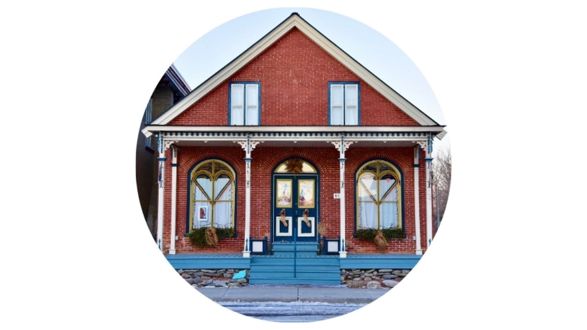 Historic red brick heritage building with a blue entrance porch, decorative trim, and arched windows, shown in a circular image.