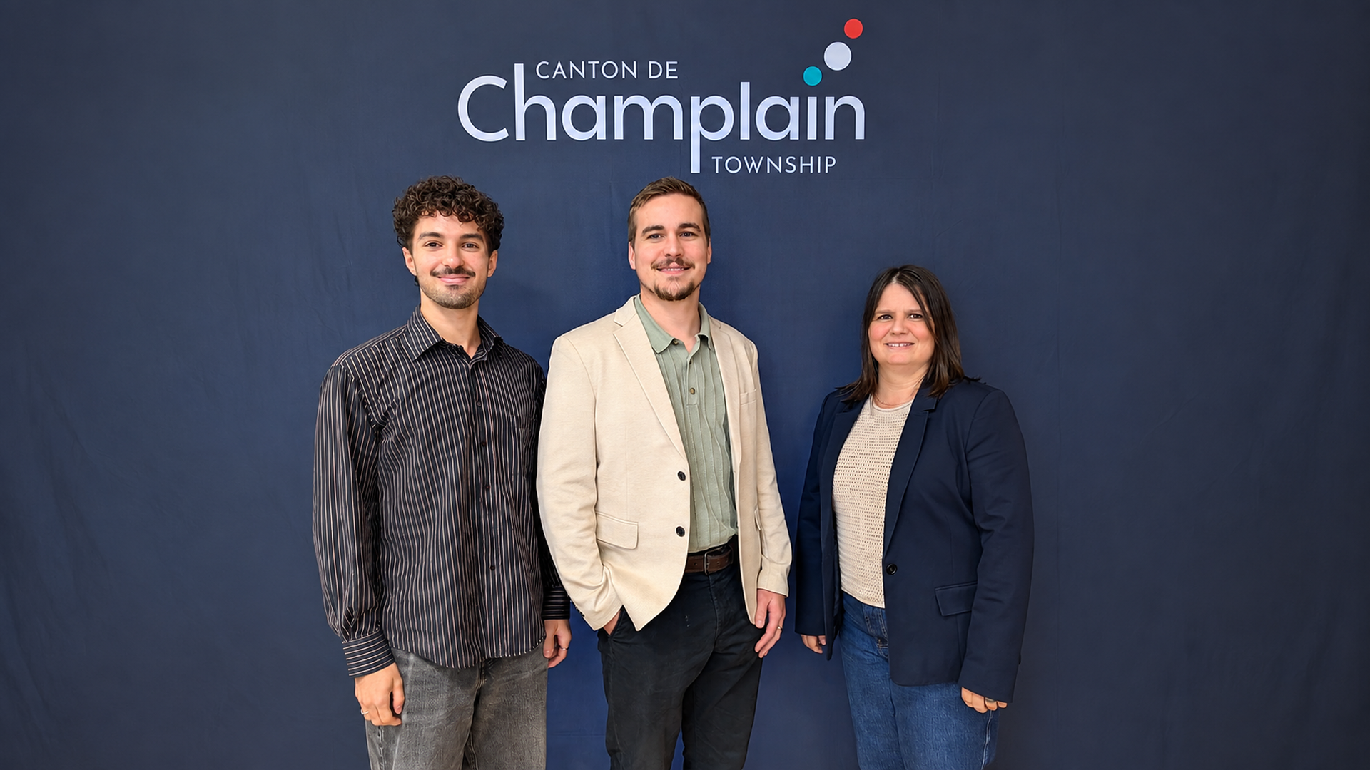 three people standing side by side in front of a dark blue background. The logo and text “Canton de Champlain Township” appear above them.