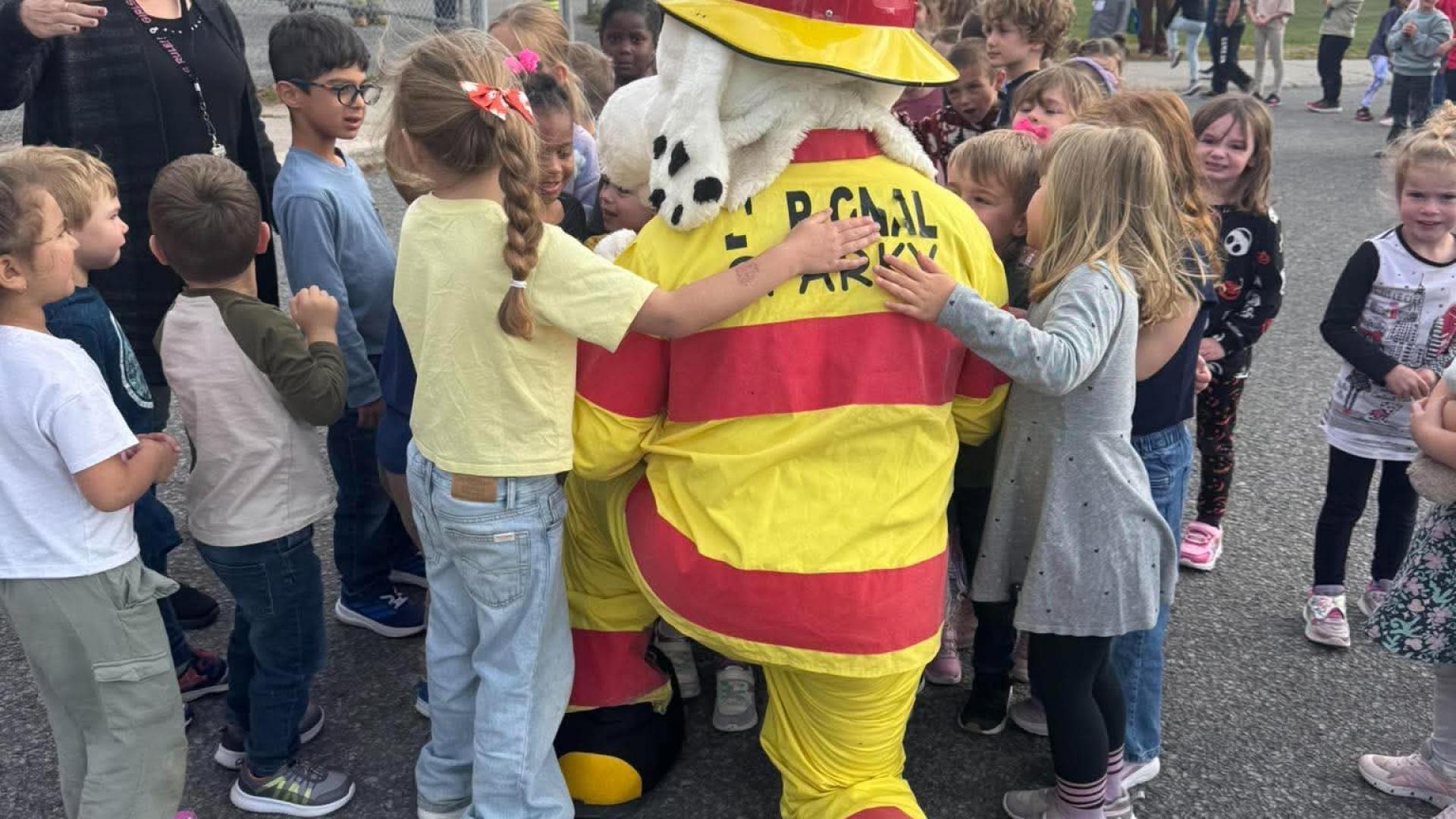 Sparky the Fire Dog kneeling in a schoolyard with a group of children