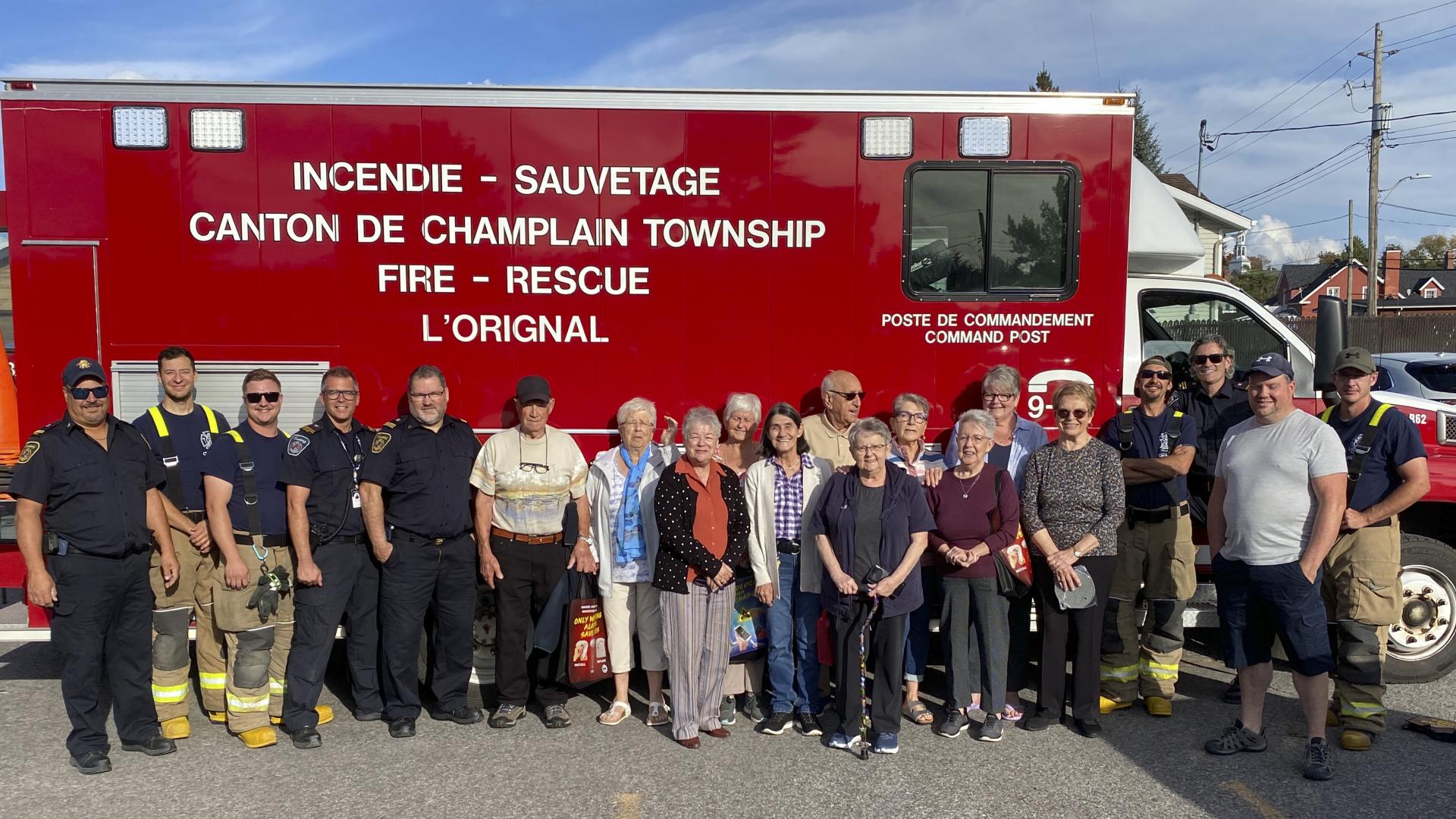 A group of adults and firefighters standing in front of a red fire truck.