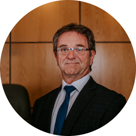 A person in a suit stands smiling in a wood-panelled office setting.