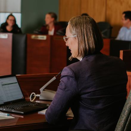 a women taking notes on a computer during a meeting that you can see in the background