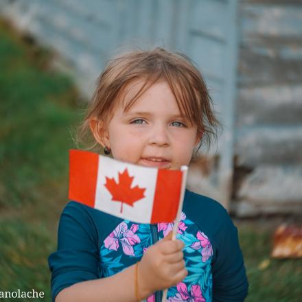 a little girl holding a canadian flag in a park