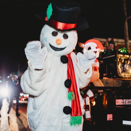 snowman mascot wandering the street during an evening christmas parade.