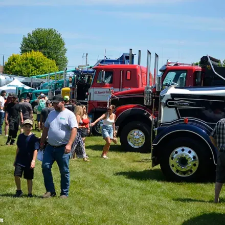 Parked trucks on a field with people looking at it.
