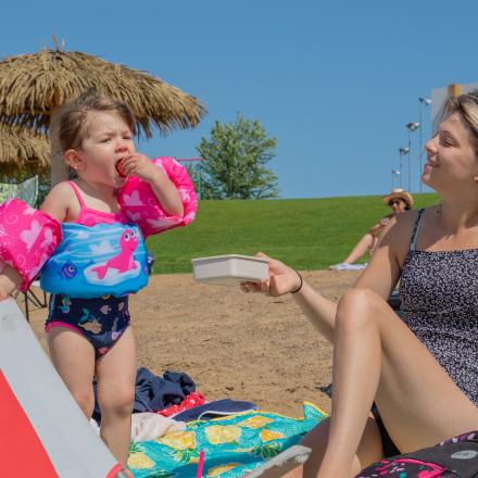 toddler in swimsuit eating grapes with her family on the beach