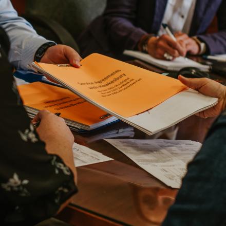 People gathered around a table reviewing and exchanging documents during a meeting