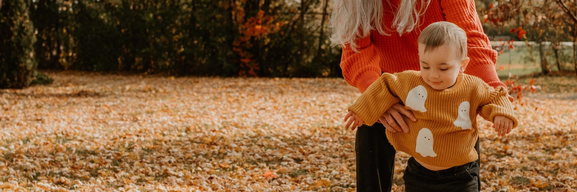 Two young children playing together in a park covered in autumn leaves.