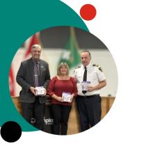 Three people holding awards during a recognition ceremony, framed within a teal and black graphic design.