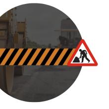 Road construction graphic featuring black and orange hazard stripes with a roadwork warning sign over a faded background of heavy construction equipment.