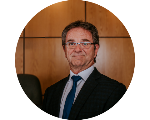 A person in a suit stands smiling in a wood-panelled office setting.