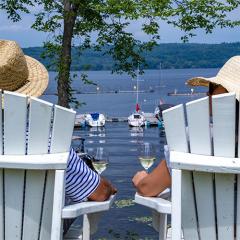 Two people in sunhats relax in chairs by a lakeside, with boats in the background.