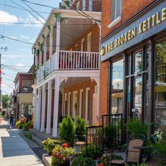 Sidewalk with vibrant flowers, historic brick buildings, and "The Broken Kettle" café.