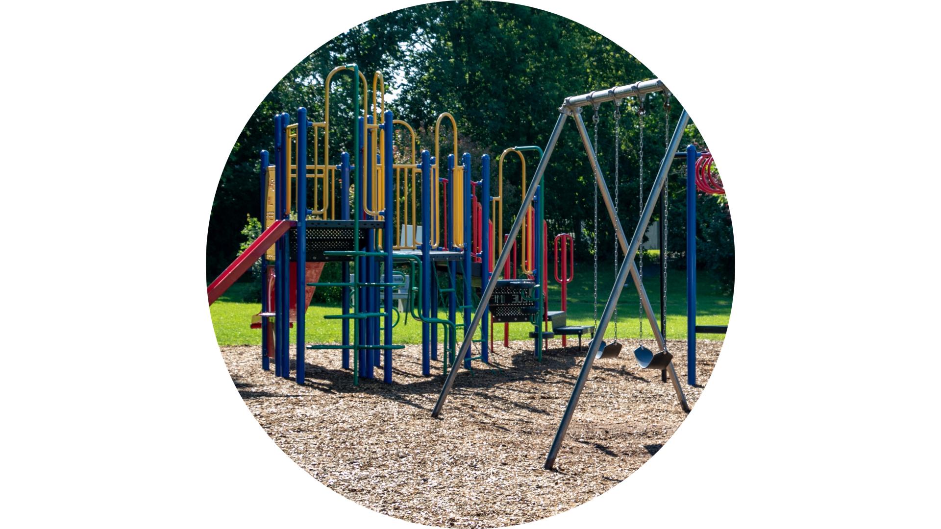 Structure de jeux colorée comprenant des glissades et des modules d'escalade dans un parc, entourée d'arbres et recouverte d'un revêtement de copeaux de bois.