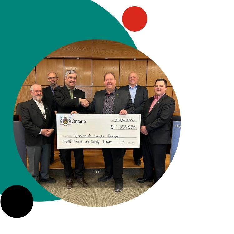 Seven people hold a large cheque in a formal setting with a Canadian flag.